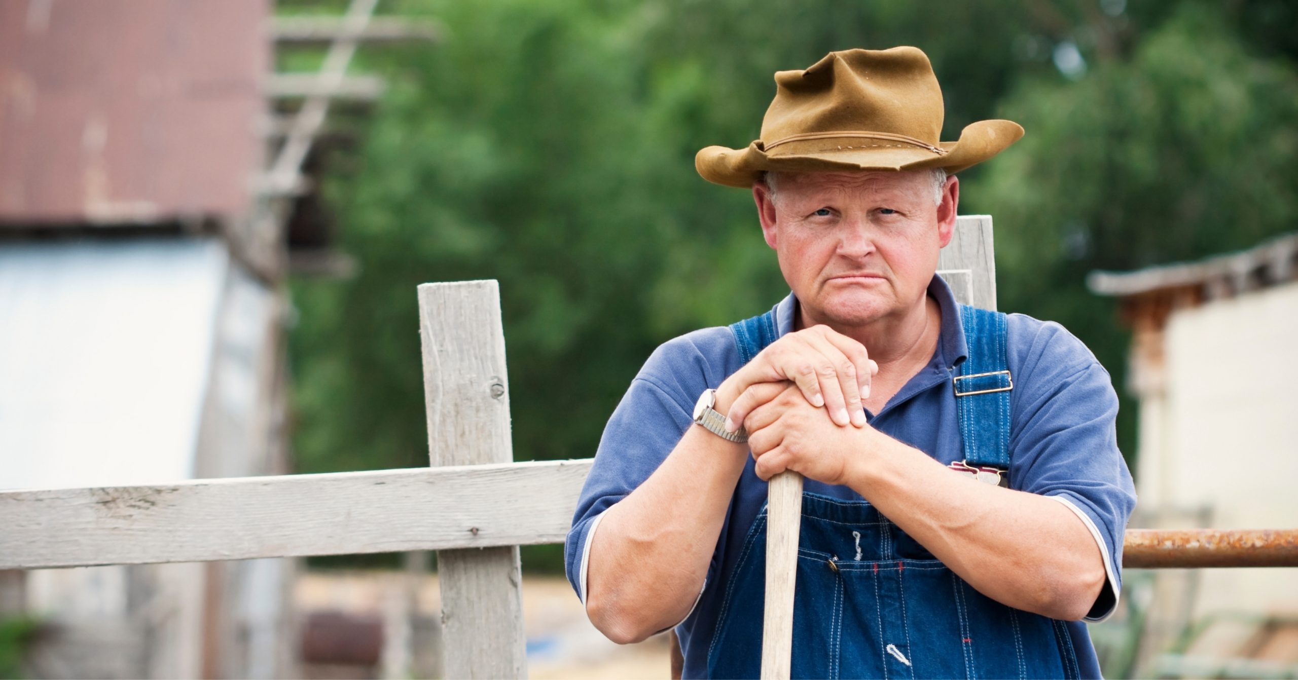 A white farmers standing with a pole in his hand.